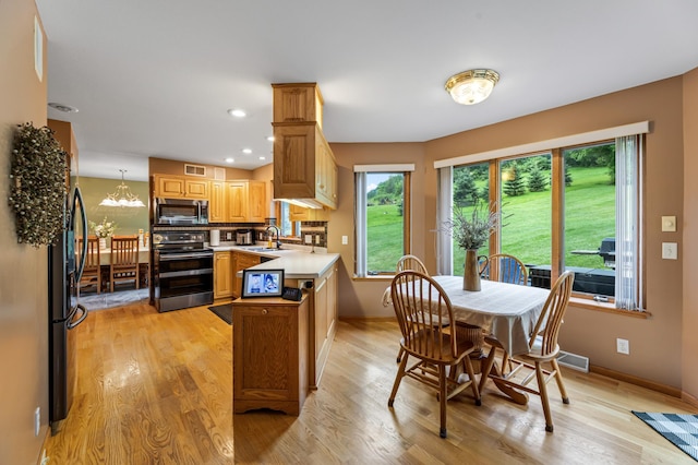 kitchen featuring stainless steel microwave, light wood-style flooring, range with electric stovetop, a peninsula, and a sink