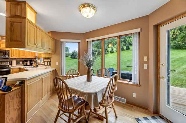 dining room featuring light wood-style floors, a healthy amount of sunlight, visible vents, and baseboards