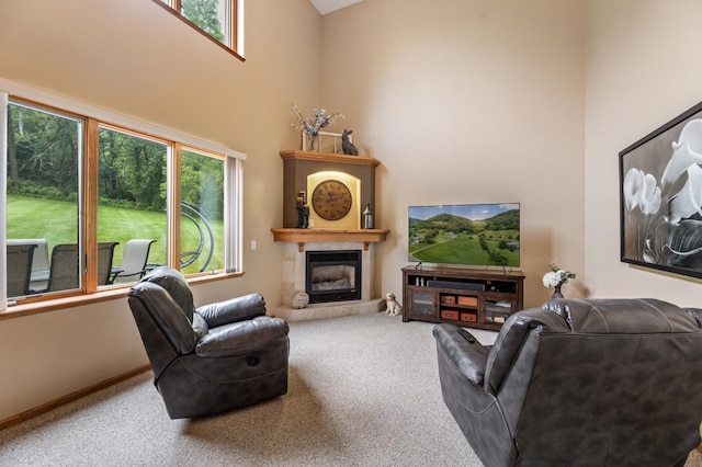 living room with a tiled fireplace, carpet flooring, baseboards, and a towering ceiling