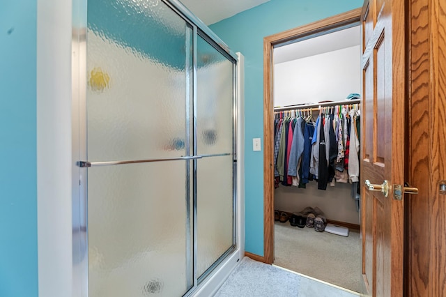 bathroom with a walk in closet, a shower stall, and baseboards