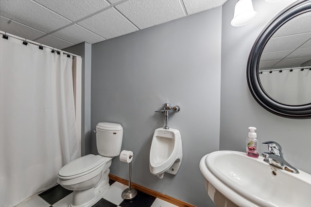 bathroom featuring a shower with shower curtain, baseboards, a drop ceiling, a sink, and toilet