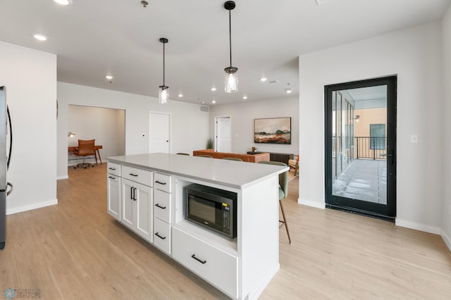 kitchen featuring a center island, white cabinets, light wood finished floors, built in microwave, and hanging light fixtures