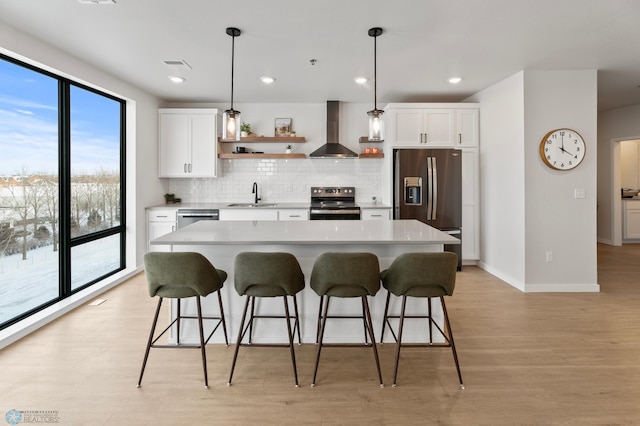 kitchen with a breakfast bar area, a sink, appliances with stainless steel finishes, wall chimney range hood, and backsplash