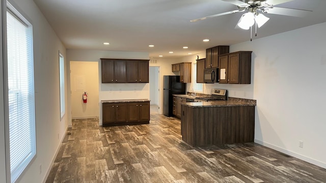 kitchen featuring ceiling fan, dark brown cabinetry, black appliances, dark stone counters, and dark hardwood / wood-style flooring