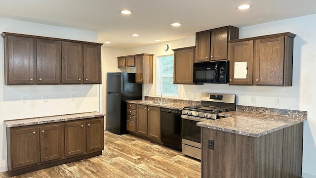 kitchen with light wood-type flooring, black appliances, dark brown cabinetry, dark stone counters, and sink