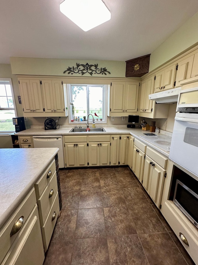 kitchen featuring dark tile patterned floors, oven, sink, cream cabinetry, and dishwashing machine