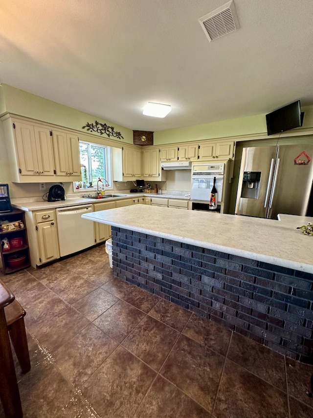 kitchen with dark tile patterned flooring, white appliances, cream cabinetry, and sink