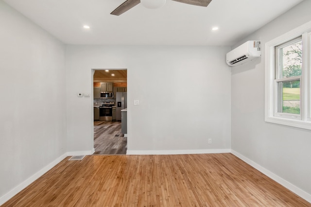 empty room featuring ceiling fan, a wall unit AC, and light hardwood / wood-style flooring