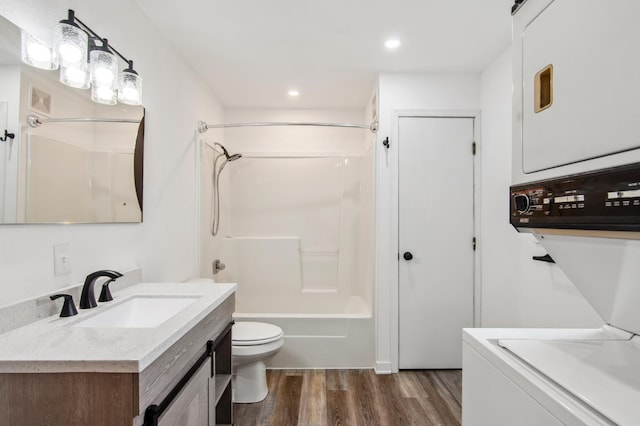 full bathroom featuring vanity, toilet, hardwood / wood-style flooring, washtub / shower combination, and stacked washer / drying machine