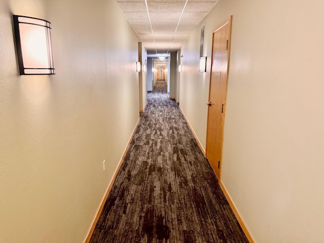 corridor with dark wood-style flooring, baseboards, and a drop ceiling