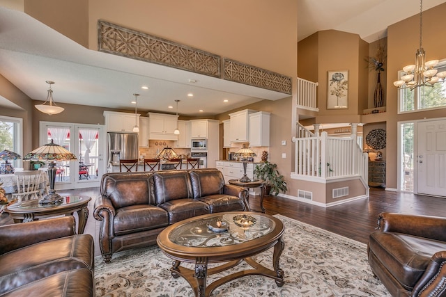 living room with french doors, a notable chandelier, a towering ceiling, and hardwood / wood-style floors