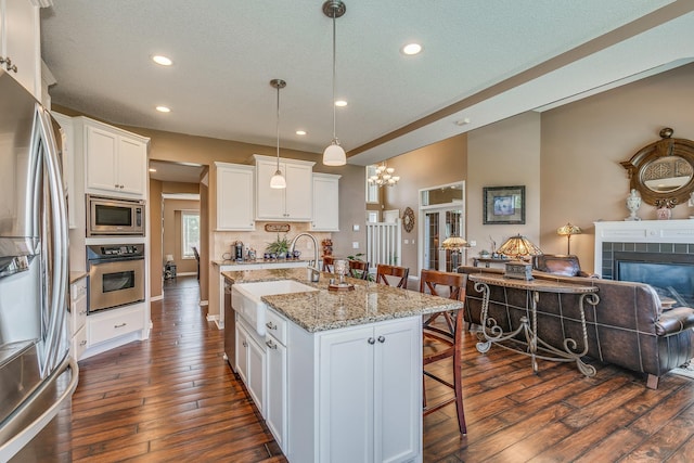 kitchen with sink, a center island with sink, white cabinetry, appliances with stainless steel finishes, and a breakfast bar area