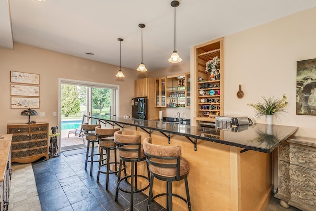 bar featuring black fridge, dark stone counters, hanging light fixtures, and sink