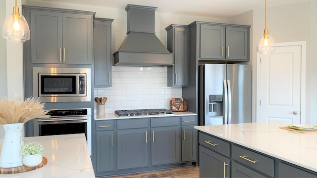 kitchen featuring decorative light fixtures, light stone counters, stainless steel appliances, and custom range hood