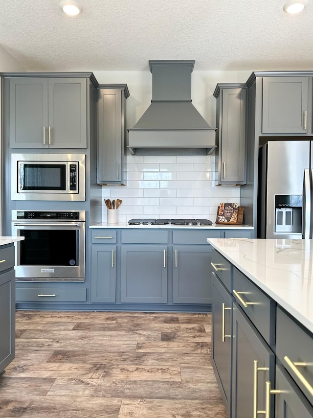 kitchen featuring stainless steel appliances, gray cabinetry, hardwood / wood-style floors, and premium range hood