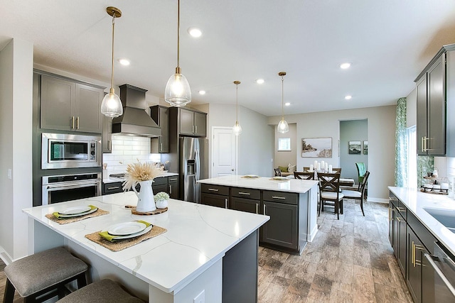 kitchen with a center island, decorative light fixtures, hardwood / wood-style floors, appliances with stainless steel finishes, and premium range hood