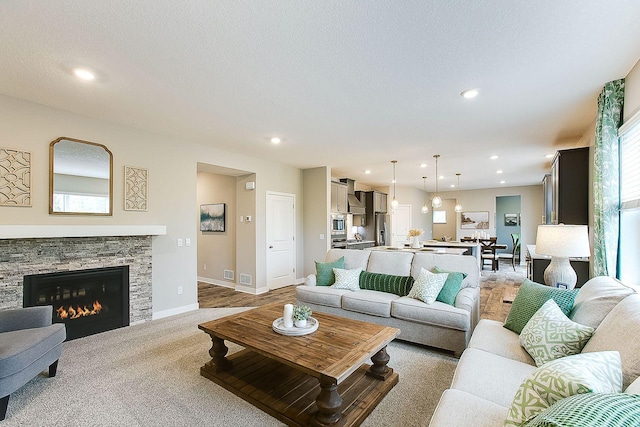 living room featuring a textured ceiling, plenty of natural light, a stone fireplace, and light carpet