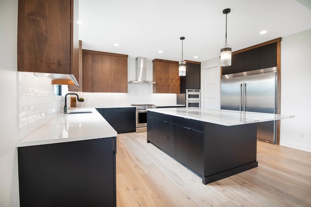 kitchen featuring appliances with stainless steel finishes, wall chimney range hood, pendant lighting, a kitchen island, and sink