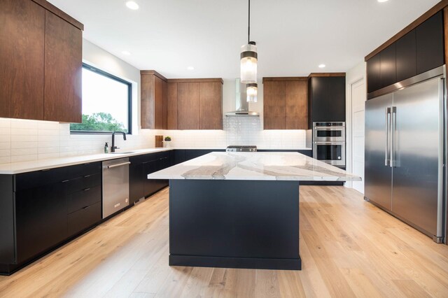 kitchen featuring wall chimney range hood, decorative backsplash, light hardwood / wood-style flooring, decorative light fixtures, and stainless steel appliances