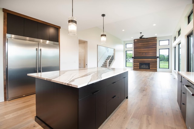 kitchen with a kitchen island, a large fireplace, decorative light fixtures, light hardwood / wood-style floors, and stainless steel built in fridge