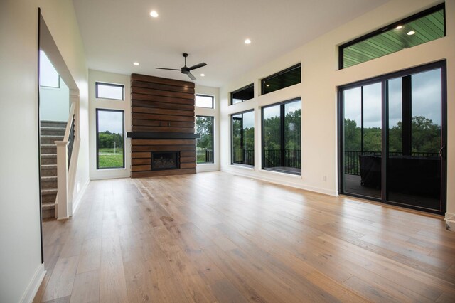 unfurnished living room featuring light wood-type flooring, a large fireplace, and ceiling fan