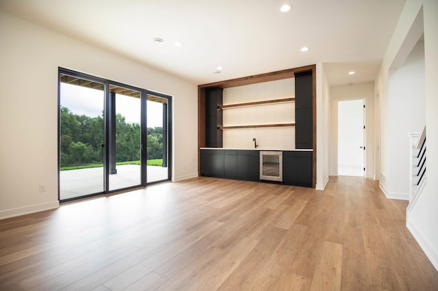 unfurnished living room featuring light wood-type flooring, beverage cooler, and indoor bar