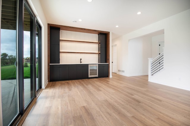 unfurnished living room featuring light hardwood / wood-style floors, beverage cooler, and bar