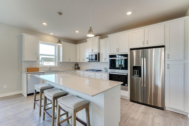 kitchen with light hardwood / wood-style floors, a center island, white cabinets, sink, and appliances with stainless steel finishes