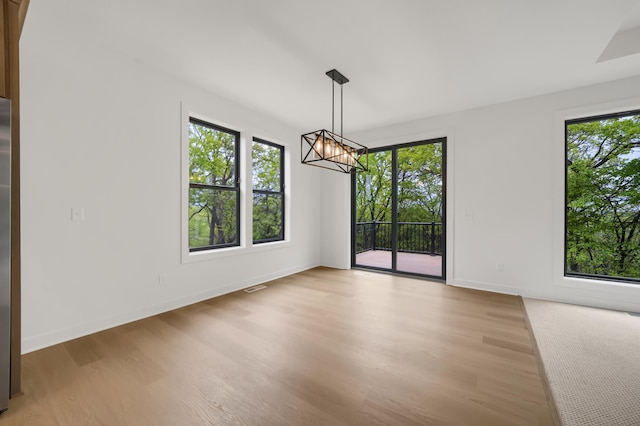 unfurnished dining area featuring a wealth of natural light, a chandelier, and light wood-type flooring