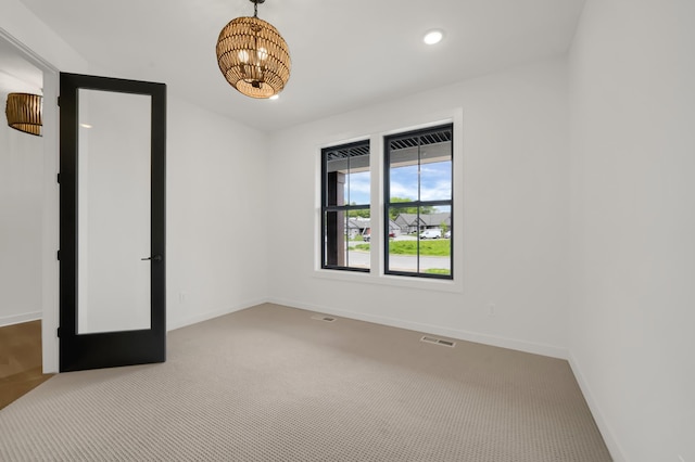 carpeted spare room featuring a notable chandelier and french doors