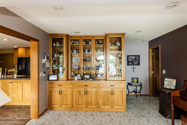 bar featuring light wood-type flooring, a textured ceiling, and black refrigerator with ice dispenser