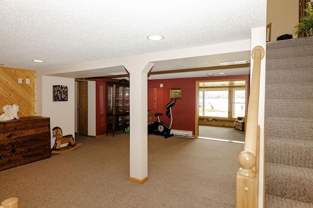 exercise room featuring a textured ceiling, wooden walls, a baseboard radiator, and carpet flooring