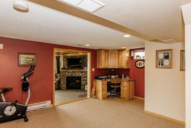 interior space featuring a baseboard heating unit, built in desk, a textured ceiling, light carpet, and a stone fireplace