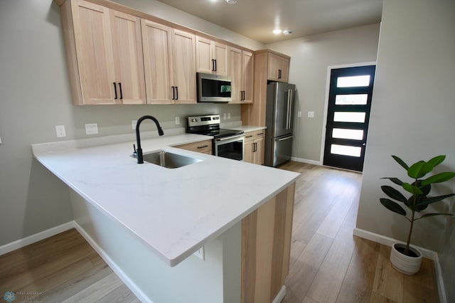 501 1st St NE, Hankinson, ND 58041 - kitchen with a sink, light brown cabinetry, light wood-style floors, stainless steel appliances, and a peninsula