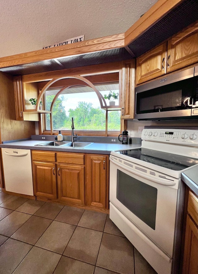 kitchen with a wealth of natural light, white appliances, dark tile patterned floors, and sink