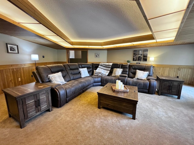 home theater with a textured ceiling, wooden walls, light colored carpet, and a raised ceiling