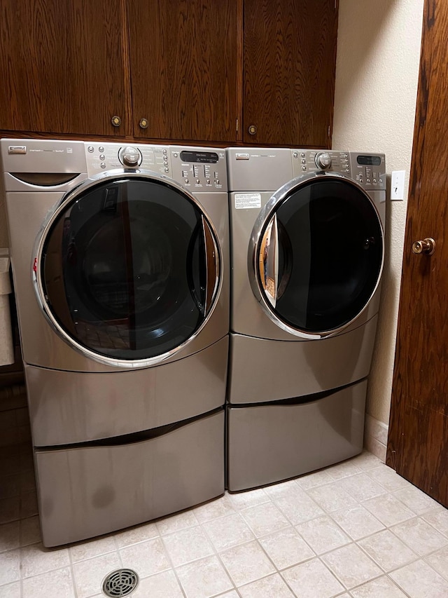 clothes washing area with washing machine and dryer, cabinets, and light tile patterned floors