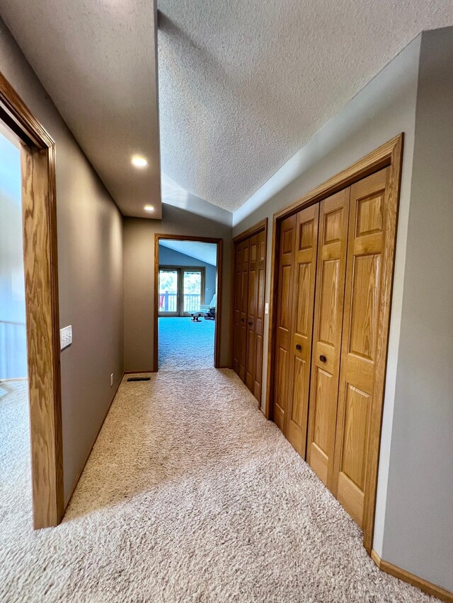 hall with light colored carpet and a textured ceiling