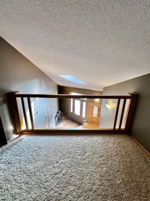 empty room with carpet flooring, lofted ceiling with skylight, and a textured ceiling