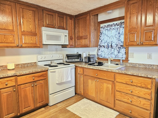 kitchen featuring light countertops, light wood-type flooring, brown cabinets, white appliances, and a sink