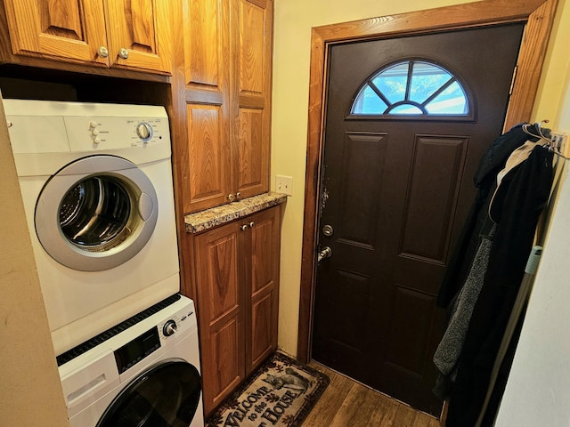 clothes washing area featuring dark wood-style floors, cabinet space, and stacked washer and dryer