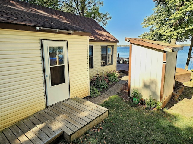 view of side of property featuring a storage unit, a water view, an outbuilding, and roof with shingles