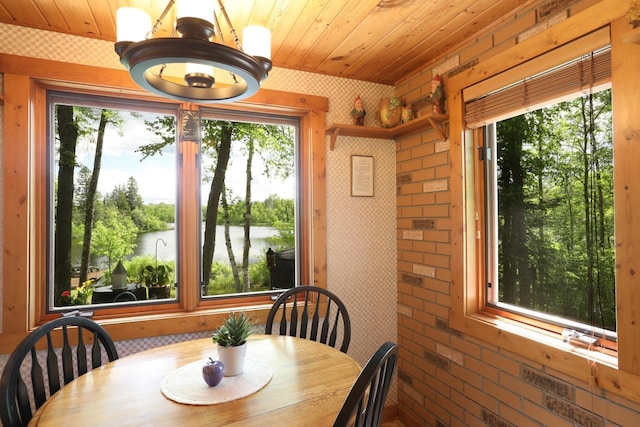 dining room with wooden ceiling, a water view, a chandelier, and brick wall