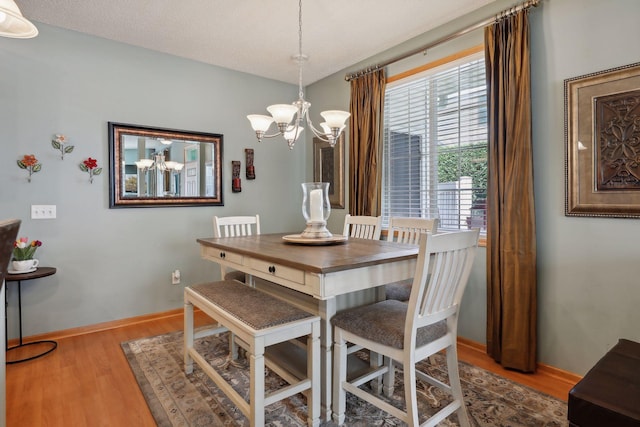 dining area with light wood-type flooring, a textured ceiling, and an inviting chandelier