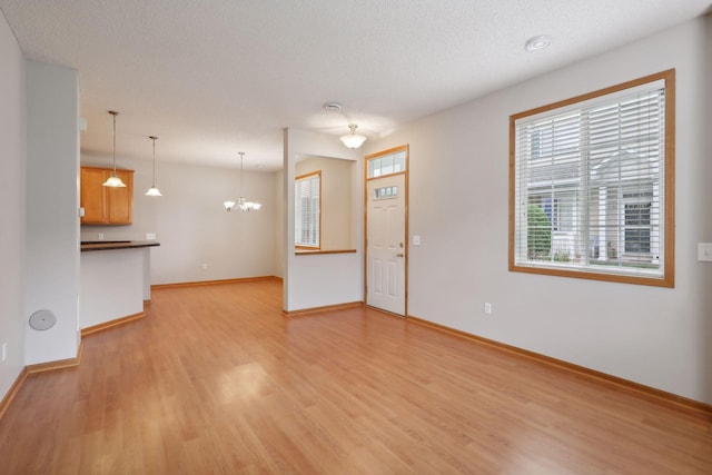 unfurnished living room with light hardwood / wood-style floors, a textured ceiling, and an inviting chandelier