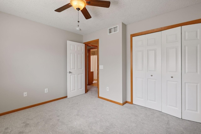 unfurnished bedroom featuring light carpet, a textured ceiling, a closet, and ceiling fan