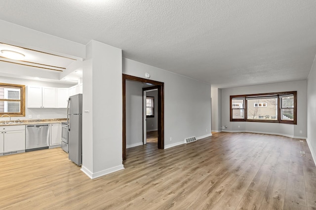 unfurnished living room with sink, light hardwood / wood-style floors, and a textured ceiling