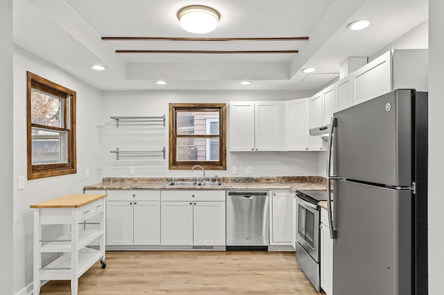 kitchen featuring sink, appliances with stainless steel finishes, white cabinetry, a tray ceiling, and exhaust hood