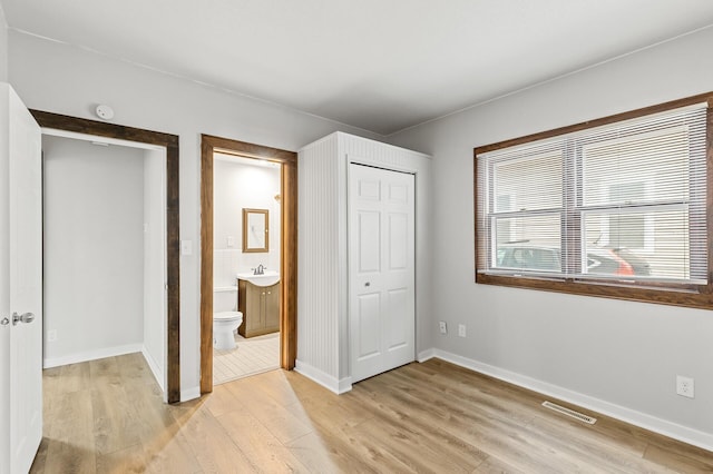 unfurnished bedroom featuring ensuite bathroom, sink, light wood-type flooring, and a closet