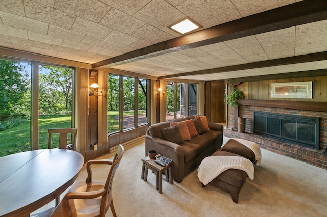 carpeted living room featuring beamed ceiling, wooden walls, a fireplace, and a healthy amount of sunlight